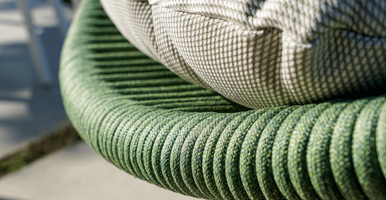 Grønn loungestol i flettet polyester med puter som egner seg for utendørsbruk